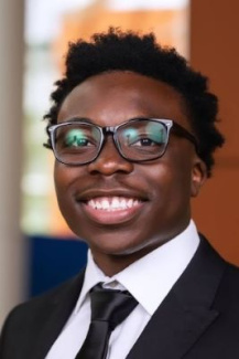 Photo of Michigan Ross student Marvin Tetteh, BBA '26, smiling and wearing a black suit with a white shirt and a black tie